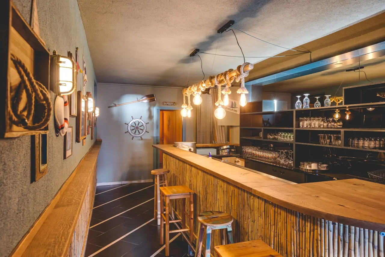 The indoor bar counter with a bamboo front, bare bulbs strung along the stone wall and a ship's wheel