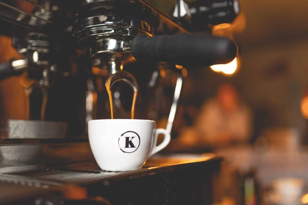 An espresso pulling into a white cup under the group head of the bar's coffee machine