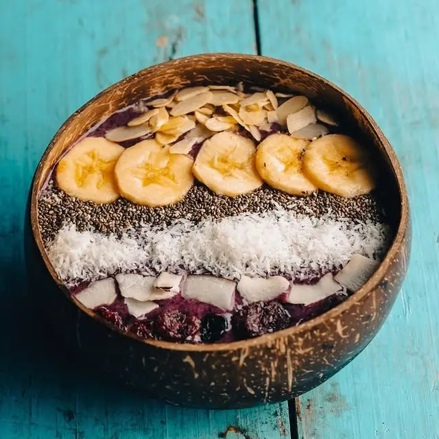 An acai bowl served in a coconut shell, topped with banana, chia seeds and coconut flakes