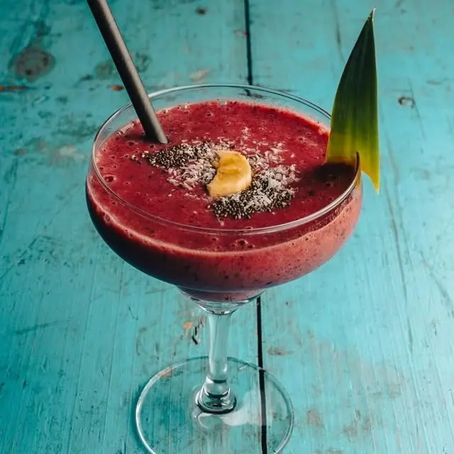 A deep red frozen berry drink in a coupe glass on the bar's teal wooden table