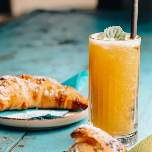 A croissant dusted with icing sugar beside a tall glass of freshly squeezed orange juice