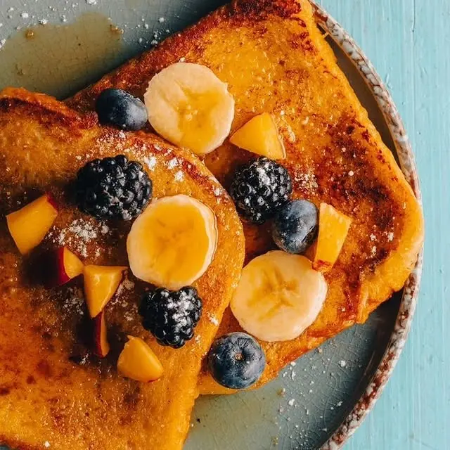 French toast topped with banana, blueberries, blackberries and mango, dusted with icing sugar