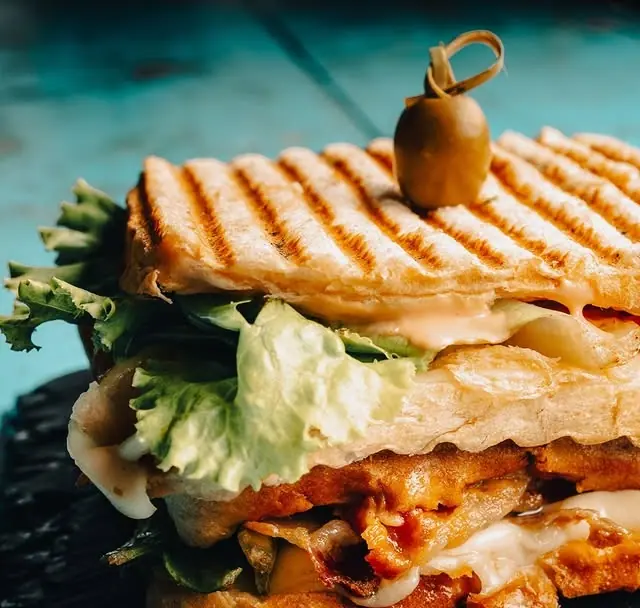 A toasted panini with melted cheese and salad, an olive pinned on top