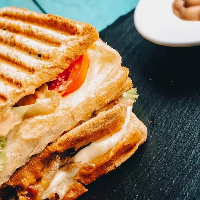 A grilled toast cut open, showing melted cheese and tomato
