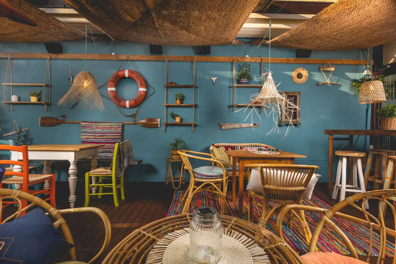 Teal interior wall with a life ring, oars, woven lampshades and a row of mismatched painted chairs