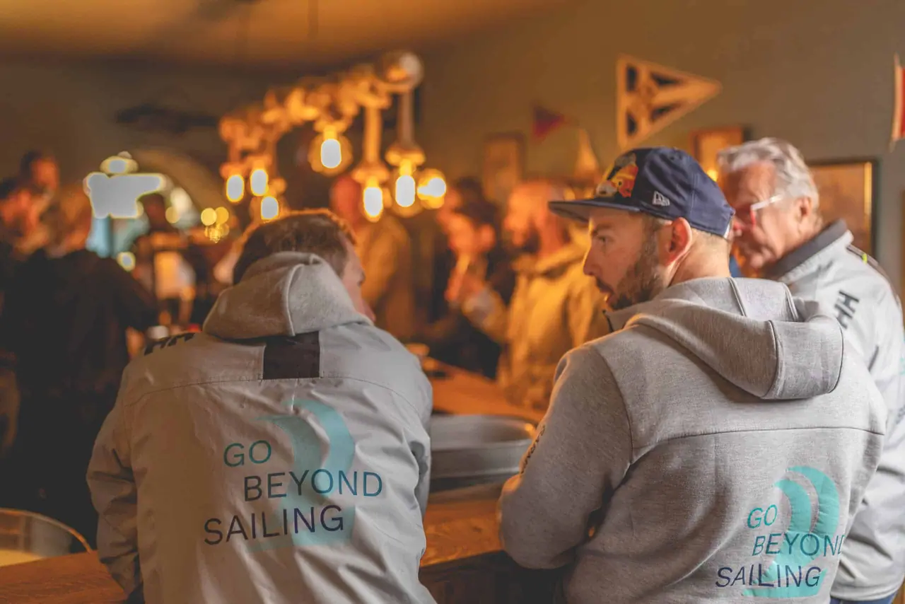 Sailing crews standing at the bar counter under warm bulbs, talking after coming off the water