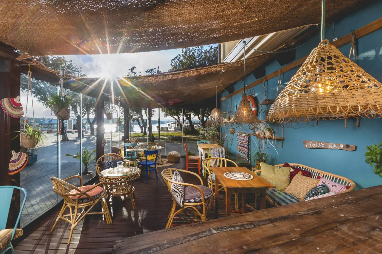 The terrace of In2 the bar at low sun, jute netting overhead, rattan lamps and mismatched chairs facing Punat marina